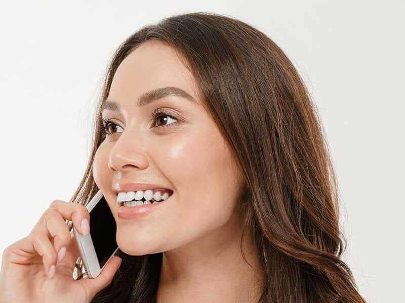 Smiling woman talking on a smartphone with clear aligners, showing how Invisalign treatment can affect speech during phone calls.