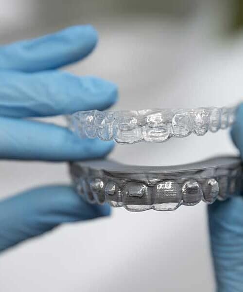 Gloved hands hold a clear plastic aligner tray above a dental mold during an Invisalign treatment refinement process assessment.